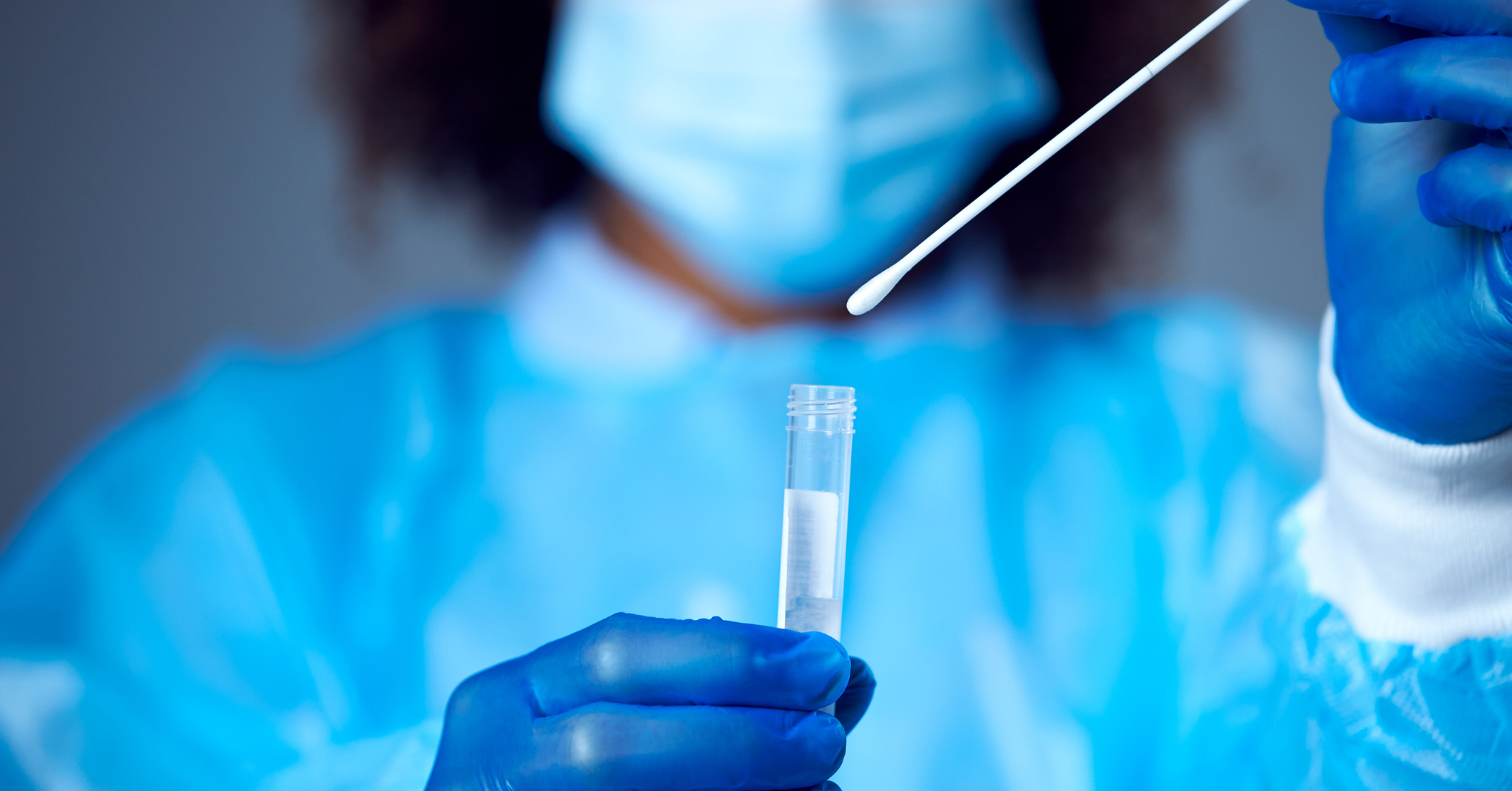 A woman out of focus wearing PPE using a swab and test tube