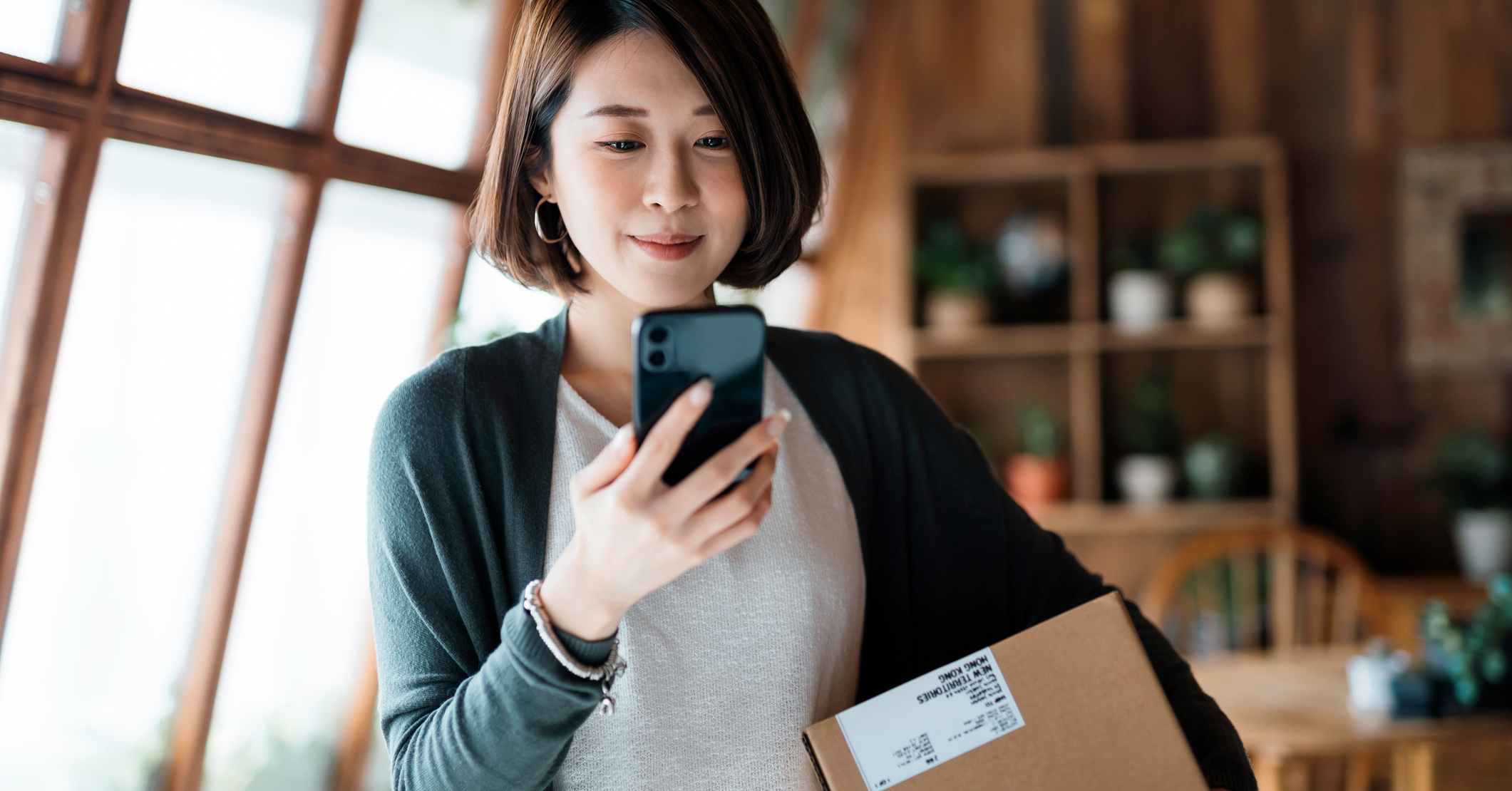 A woman with short hair smiling at her phone holding a box 