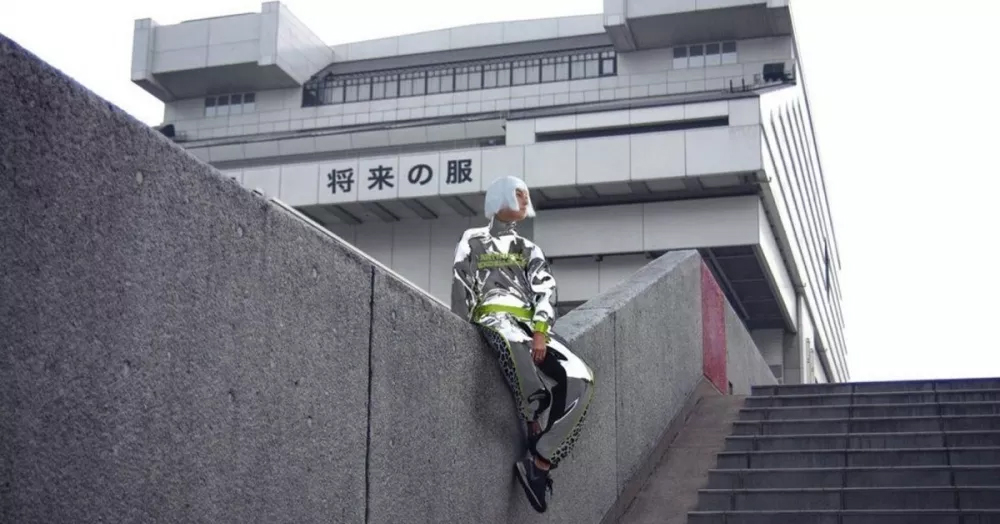 A woman with white hair sitting on a wall in front of a building
